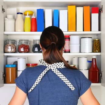 A woman seen from behind opening doors to a food cupboard.